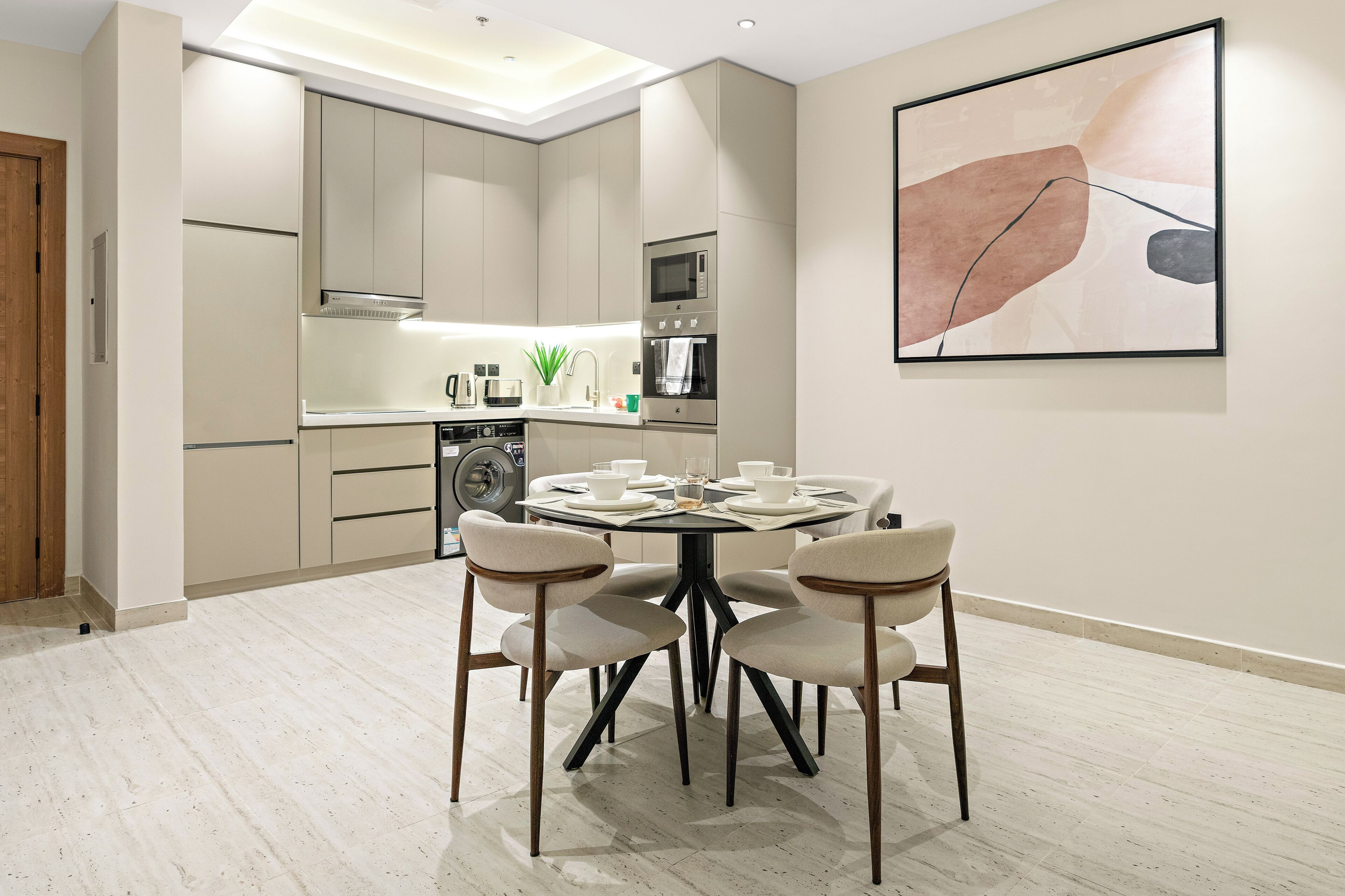 A modern kitchen with a dining area, featuring a round table with chairs, a microwave, oven, and a coffee maker.
