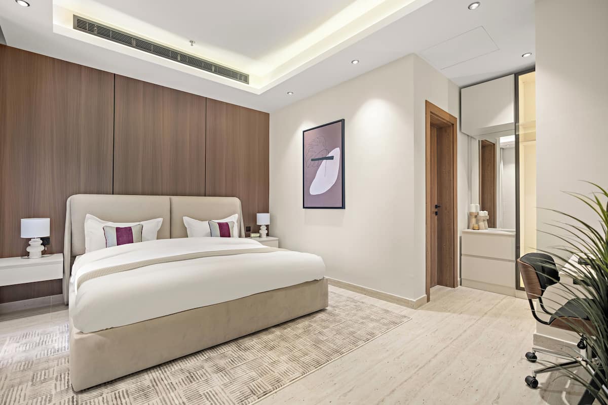 A modern bedroom with a large bed, bedside tables, a mirror, and a plant.