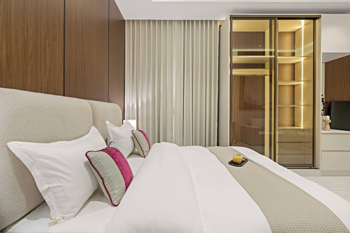A modern hotel room with a large bed, a walk-in closet, and a television.