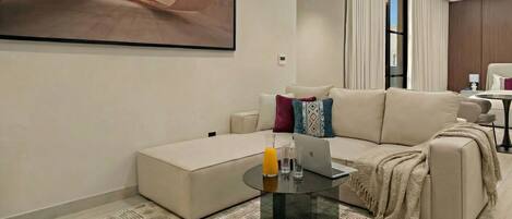 A modern living room with a sofa, a glass coffee table, a laptop, and a painting on the wall.