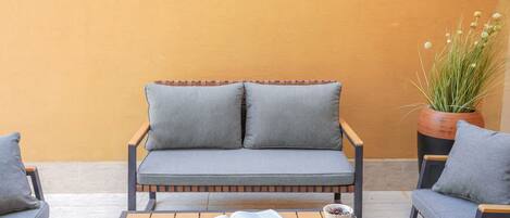 A sofa with cushions, a table with a magazine, a cup, and a potted plant.