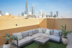 A rooftop terrace with a grey sectional sofa, a small table, and potted plants. - LIV by Yamama - KAFD (Riyadh)