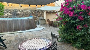 Ein Außenbereich mit einer Terrasse, einem runden Tisch und Stühlen, einer Steinmauer und einem Wasserspiel.