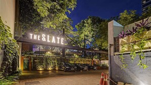 Außenansicht von 'The Slate' mit modernem Design, einschließlich einer gut sichtbaren Beschilderung, einem Parkplatz und umgebender Bepflanzung.