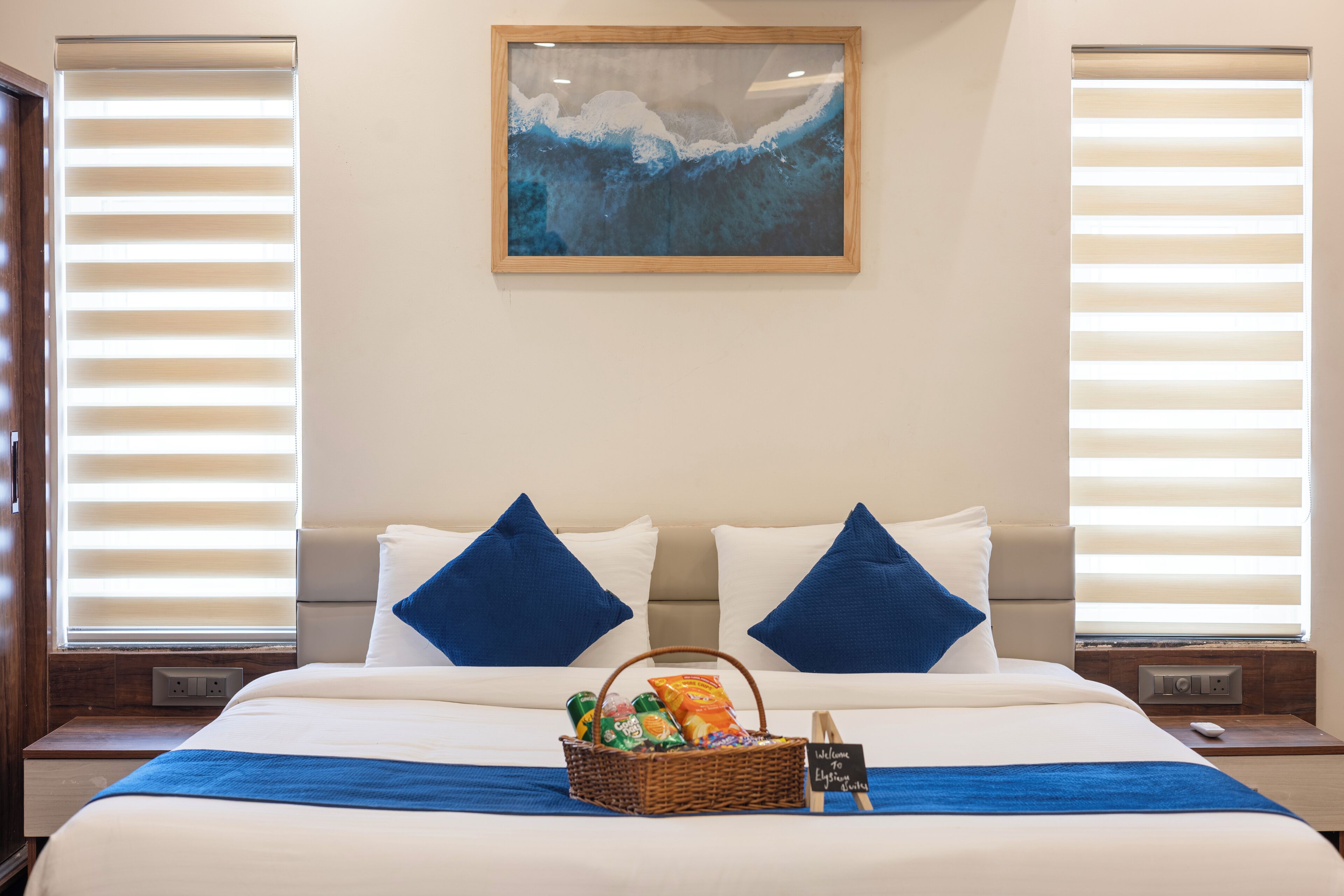 A hotel room with a bed, a basket of snacks, and a welcome sign.