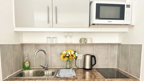 Une cuisine moderne dotée d’un four à micro-ondes encastré, d’un évier en acier inoxydable et d’un lave-vaisselle compact.