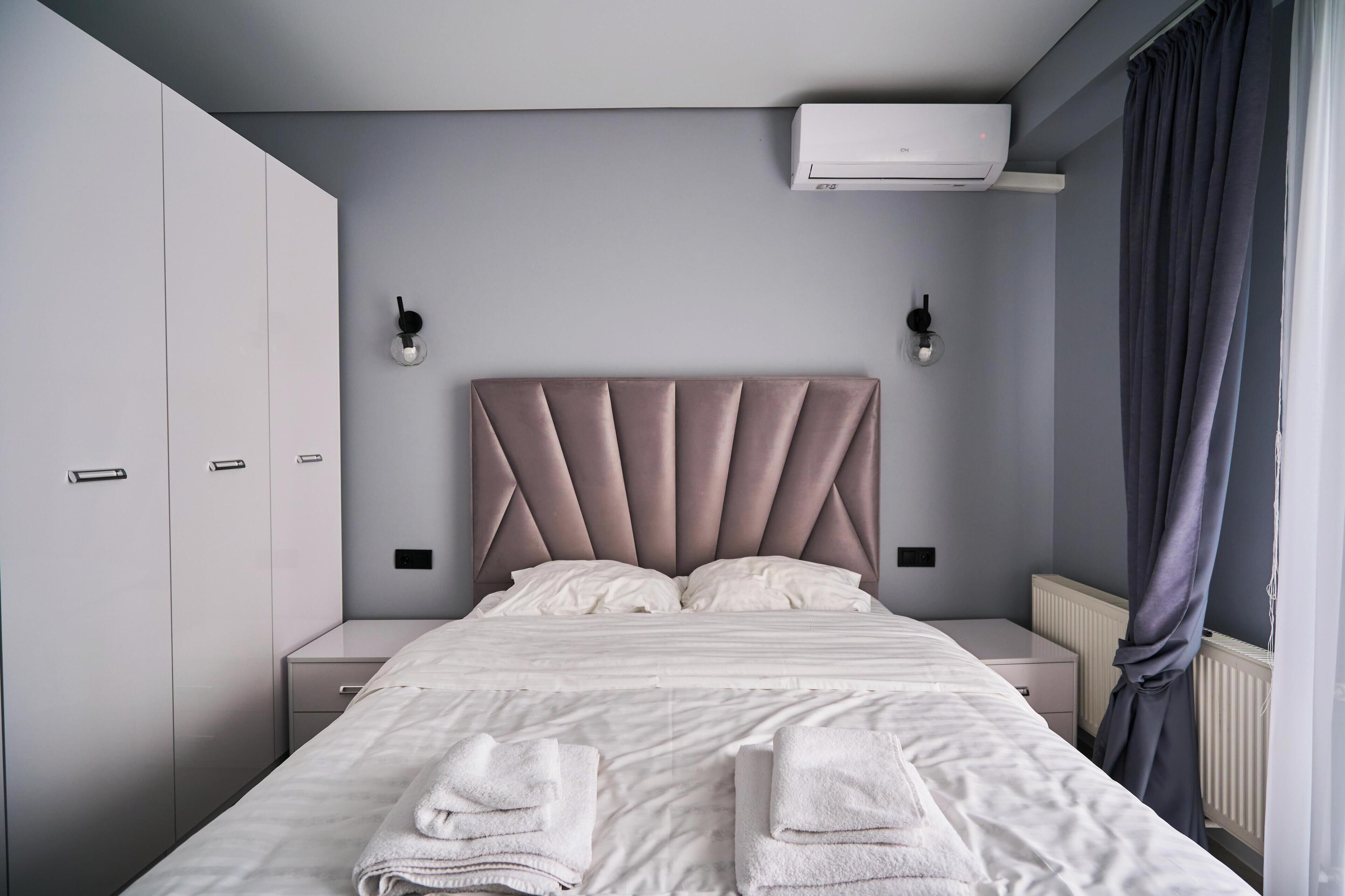 Ein modernes Schlafzimmer mit einem großen Bett, Nachttischen, einem Kleiderschrank und einer Klimaanlage.