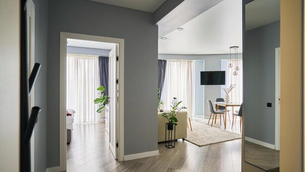 A modern living room with a sofa, dining table, and chairs. There is a TV mounted on the wall and a plant on a side table. - Modern 1BR - Balcony - in Center by Torro Mall (Chișinău)