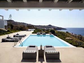 Uma área de piscina com espreguiçadeiras e vista para o mar.