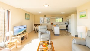 A modern living room with a flat-screen TV, a comfortable sofa, a dining area, and a kitchen with white cabinets.