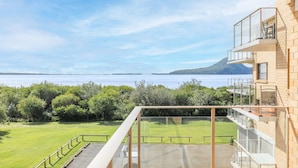 A modern building with a glass balcony overlooking a body of water and greenery.