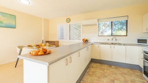 A kitchen with a central island, white cabinetry, a window with blinds, a clock, and a fruit bowl on the counter.