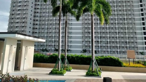 A high-rise building with a uniform facade, surrounded by palm trees and a small pool area. - BREEZE RESIDENCES MANILA BAY VIEW (Pasay)