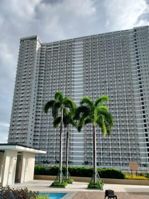 A high-rise building with a uniform facade, surrounded by palm trees and a small pool area. - BREEZE RESIDENCES MANILA BAY VIEW (Pasay)