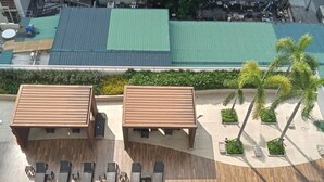A rooftop pool area with two wooden structures, lounge chairs, and a palm tree. - BREEZE RESIDENCES MANILA BAY VIEW (Pasay)