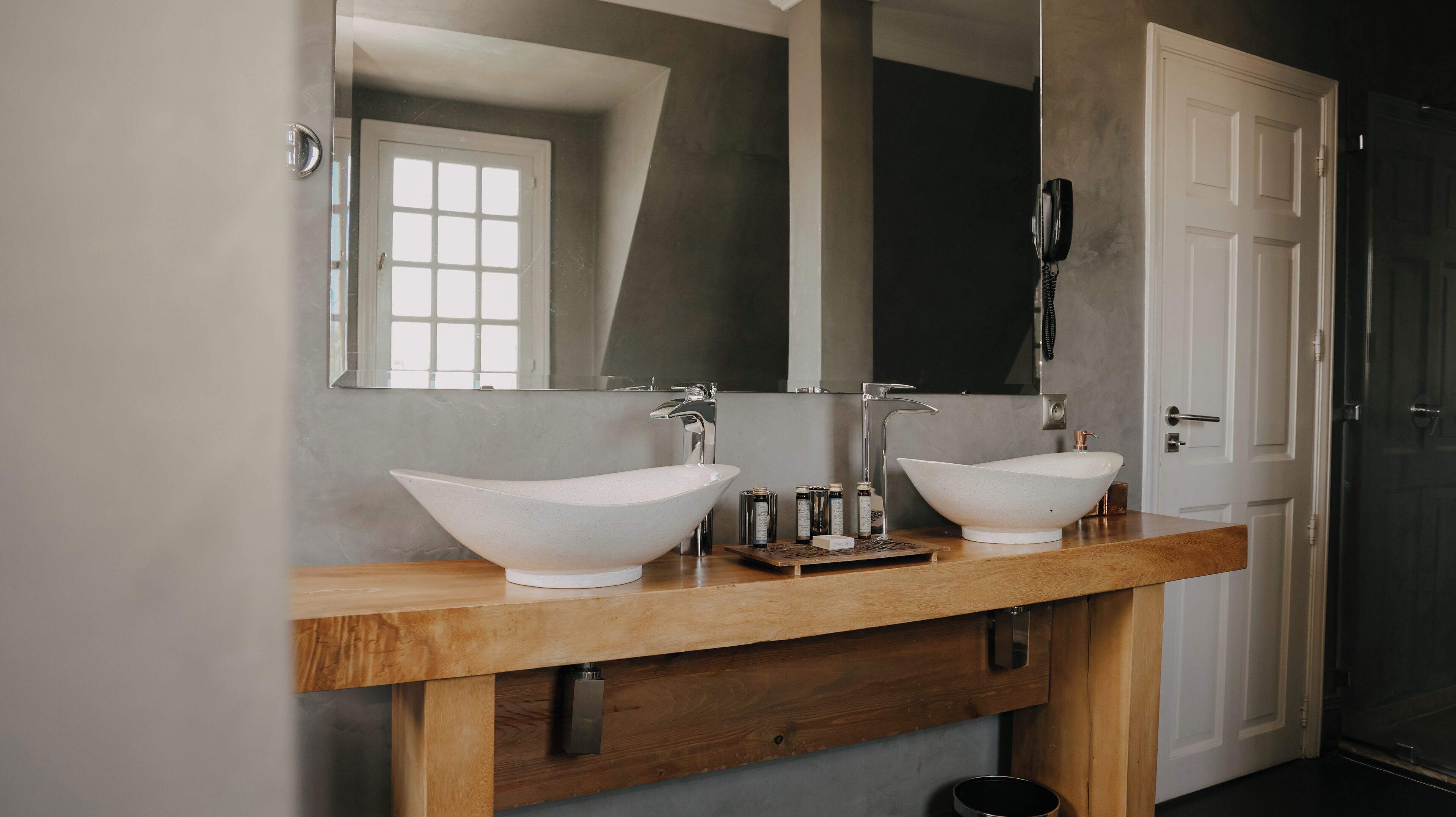 Un baño con dos lavamanos, un mueble de tocador de madera, un espejo grande y una puerta.
