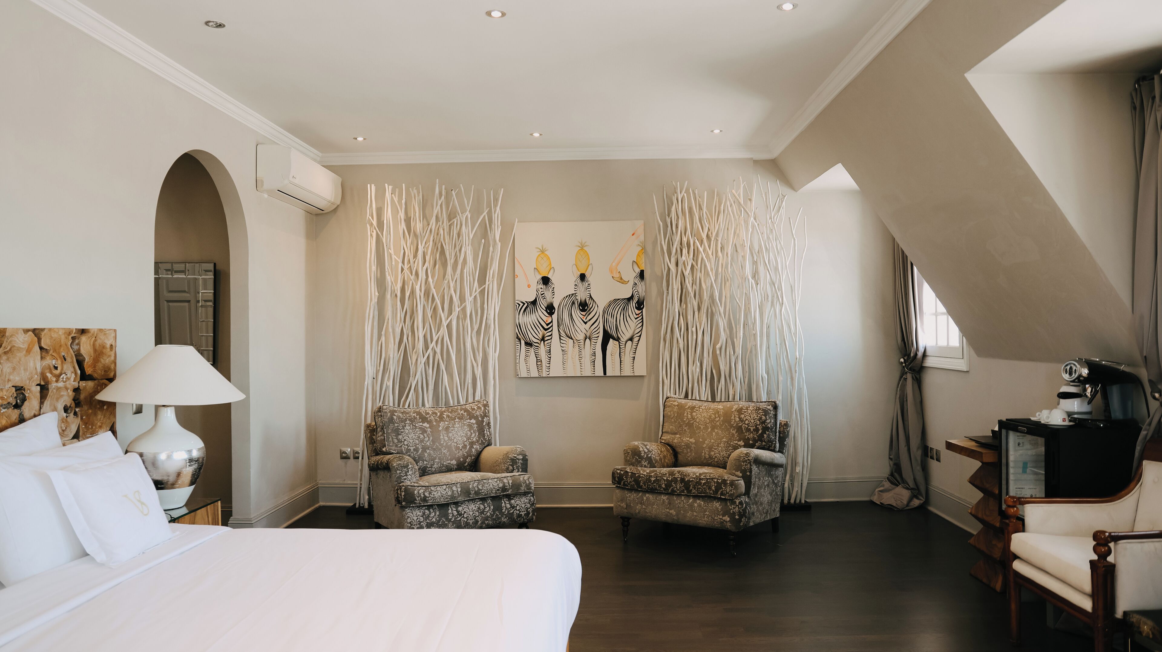 Quarto de hotel com uma cama grande, duas poltronas, um quadro e uma máquina de café.