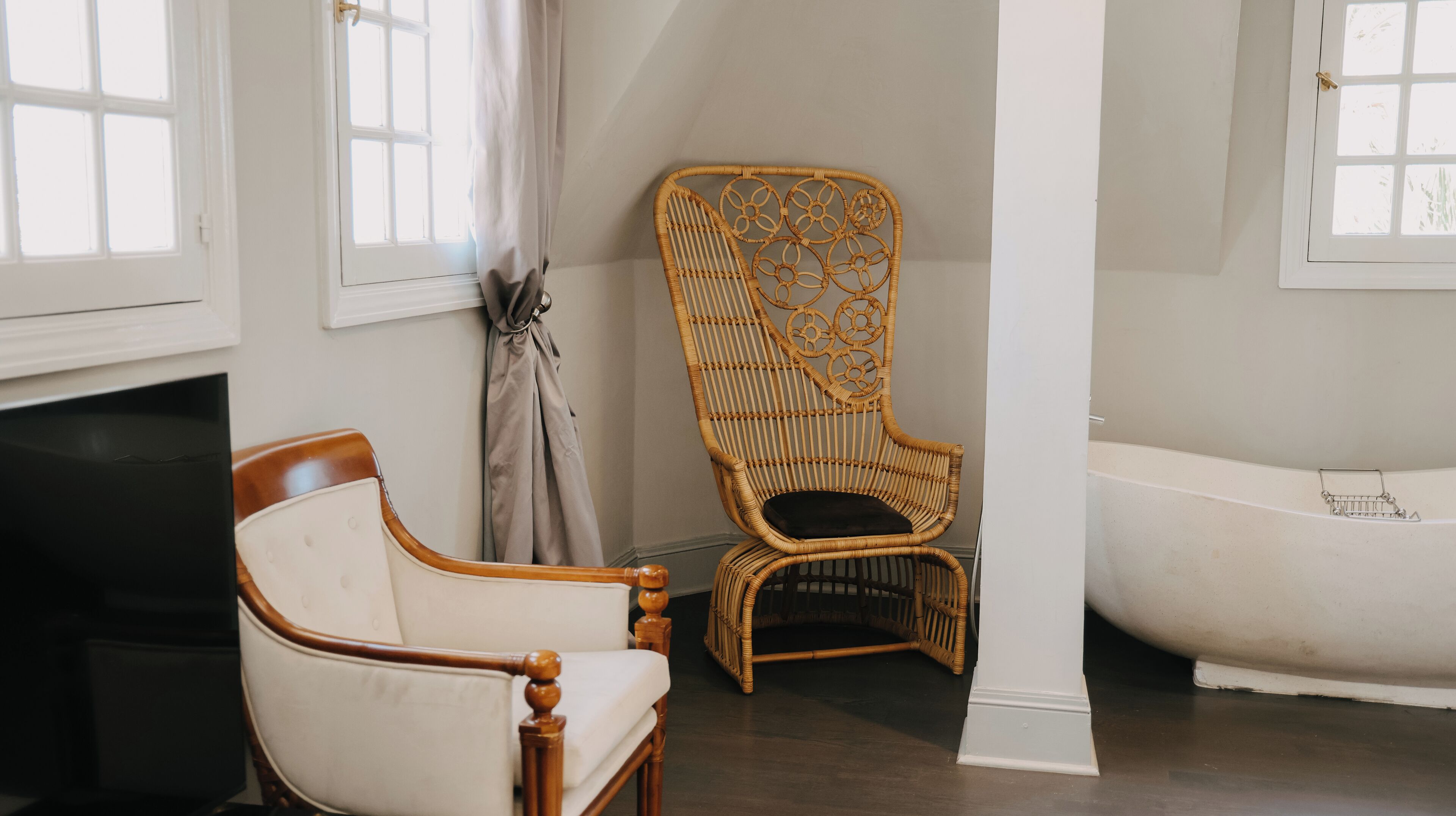 A room with a white chair, a wicker chair, and a white bathtub.