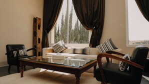 Un salon avec une table basse en verre, deux fauteuils, un canapé et une grande fenêtre avec des rideaux.