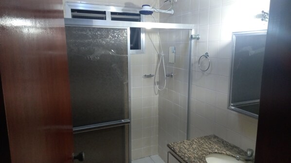 A bathroom with a glass-enclosed shower, a granite countertop sink, and a mirror.