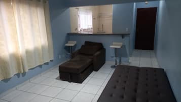 A room with blue walls, a brown sofa, a brown ottoman, two white side tables, and a mirror above a counter.