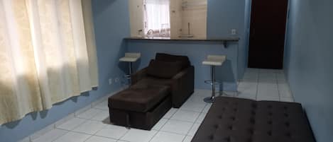 A room with blue walls, a brown sofa, a brown ottoman, two white side tables, and a mirror above a counter.