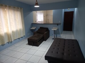 A room with blue walls, a brown sofa, a brown ottoman, two white side tables, and a mirror above a counter.