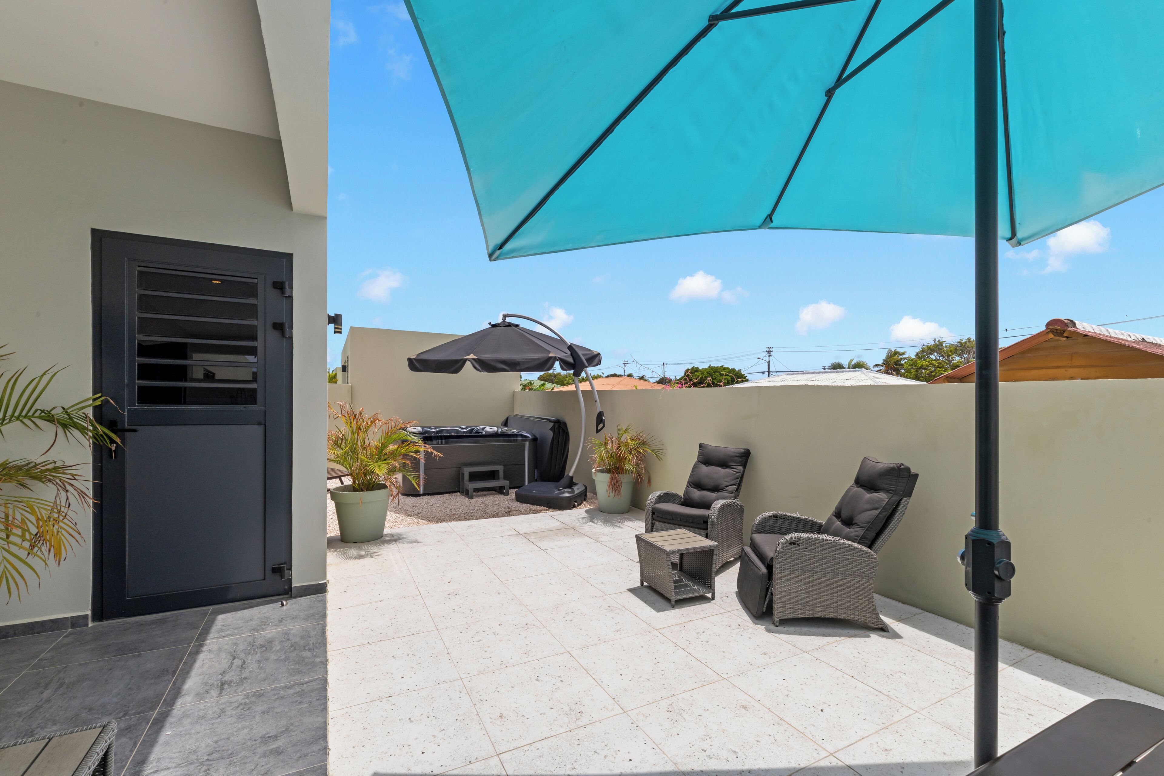 Un patio con mobiliario exterior, una parrilla y un gran paraguas.
