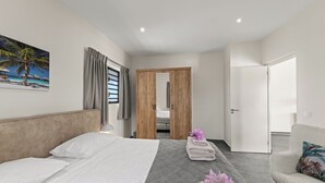 A hotel room with a bed, a chair, a door, and a painting on the wall.