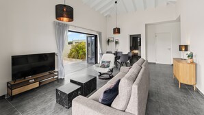 A modern living room with a flat-screen TV, a grey sofa, a coffee table, and a dining area with a chair and table.