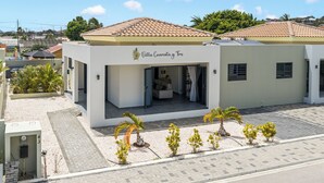 A two-story building with a tiled roof, a sign reading 'Villa Cuartita y Tres,' and a paved entrance area with small palm trees.