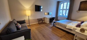 A hotel room with a bed, a desk, a chair, a sofa, a lamp, and a TV.