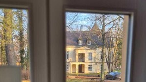 A room with a large window overlooking a grassy yard and a distant building. - Schloss Hohenbocka (Hohenbocka)