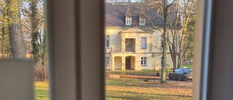 A room with a large window overlooking a grassy yard and a distant building.