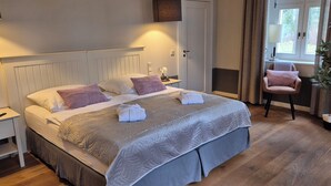 A neatly made bed with a grey bedspread and pillows, a bedside table with a lamp, a chair with a cushion, and a potted plant. - Schloss Hohenbocka (Hohenbocka)