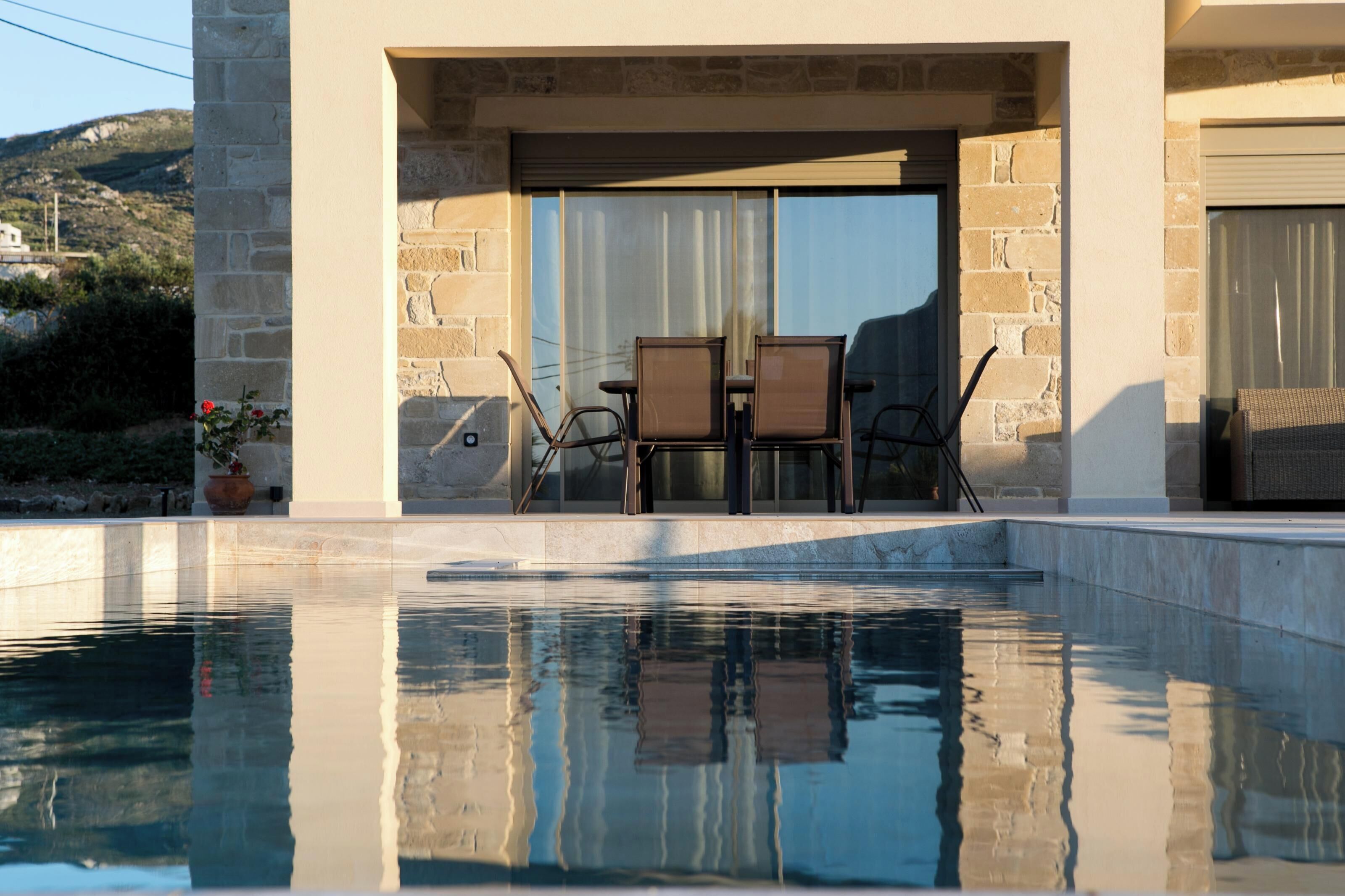 A poolside area with stone walls, a covered seating area, and a view of the surrounding landscape.