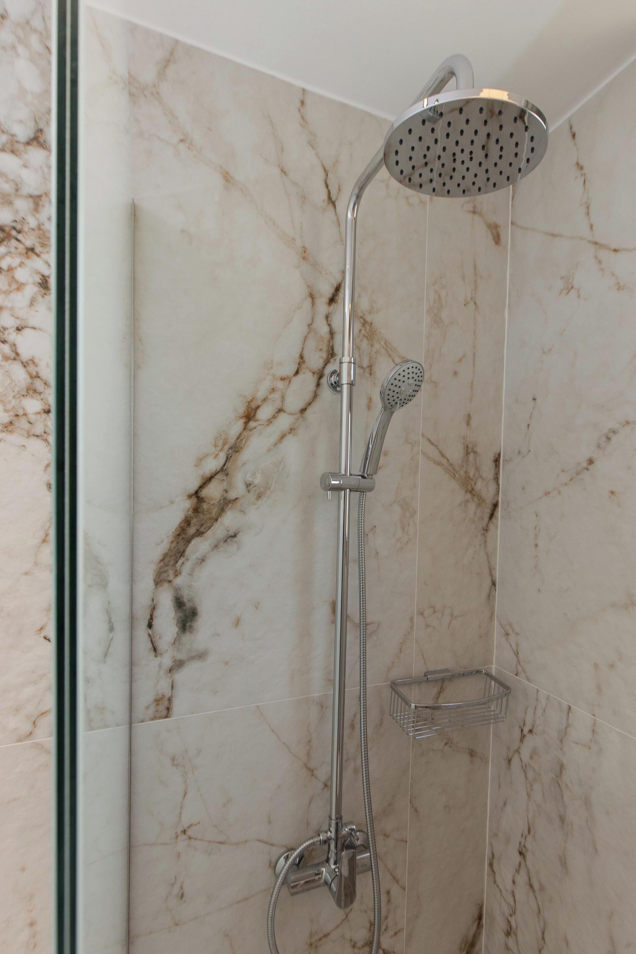 A modern shower with a handheld showerhead and a wall-mounted rain showerhead, set against a marble wall.