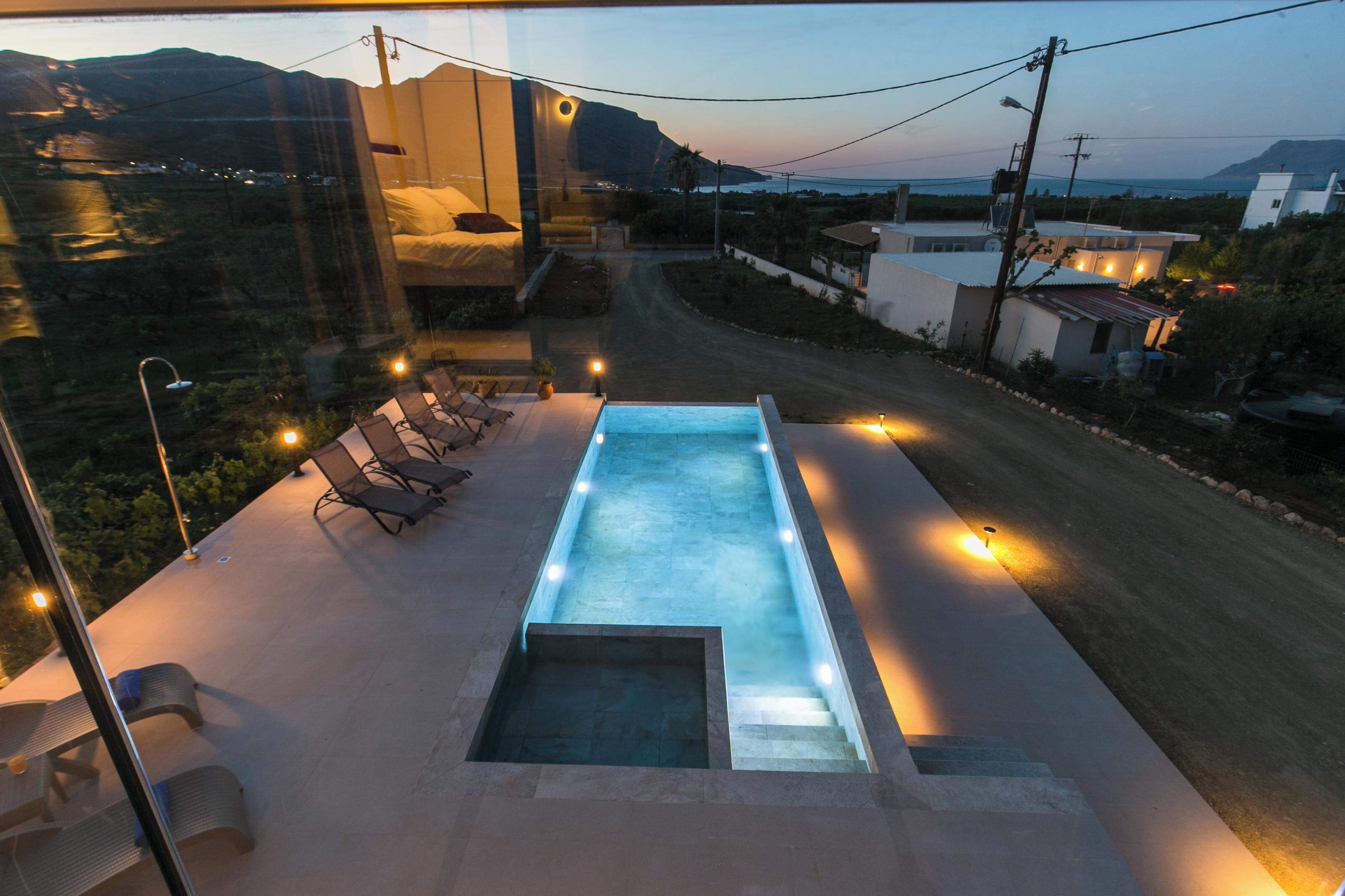 A modern outdoor pool area with a view of the surrounding landscape, including a road and distant hills.