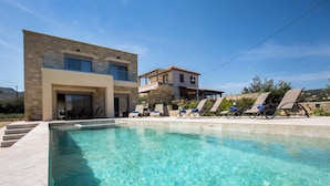A modern pool area with clear blue water, a stone building, and a second-story balcony.