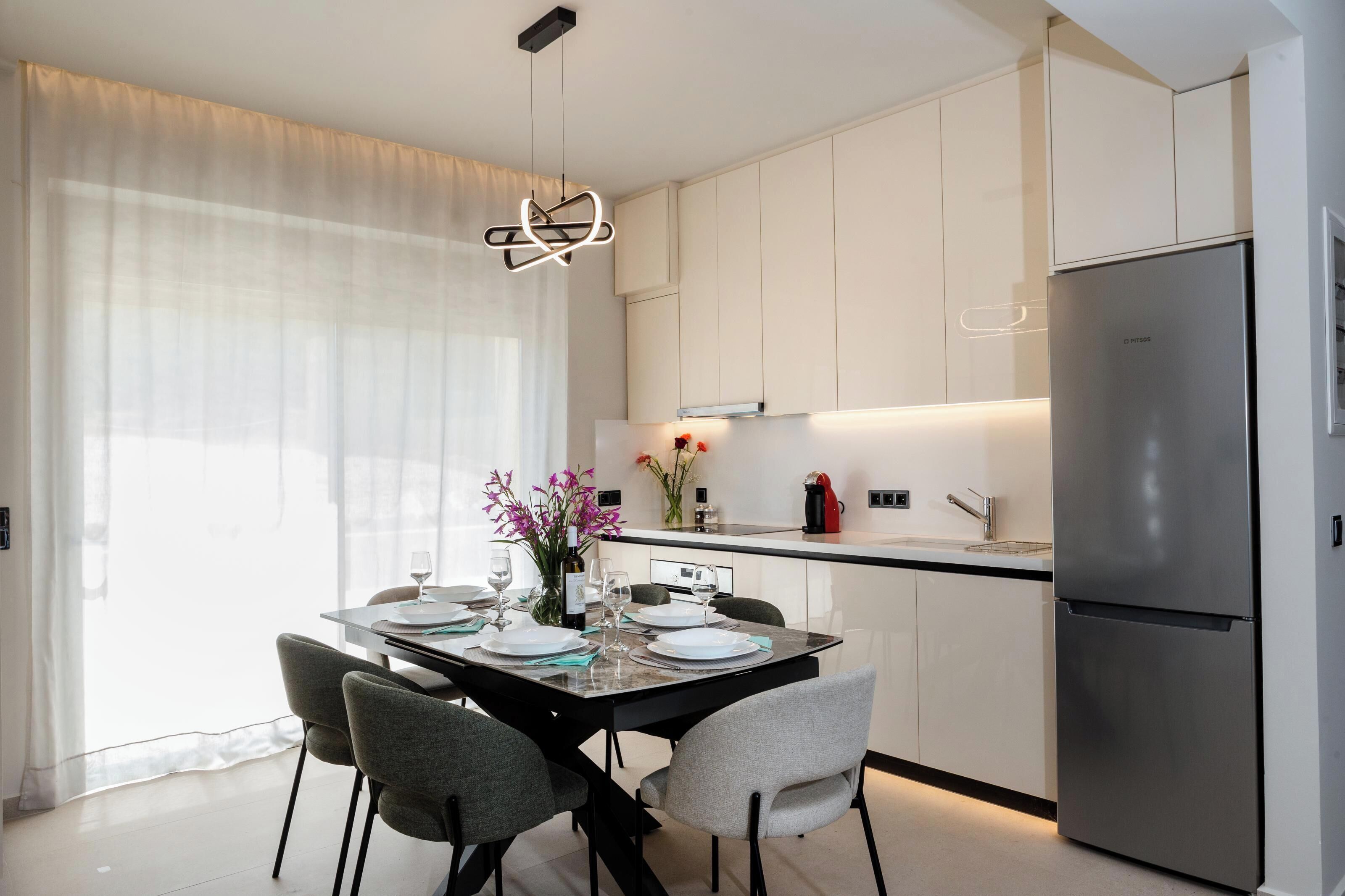 Une cuisine moderne avec des meubles blancs, un réfrigérateur en acier inoxydable et un coin repas avec une table dressée pour quatre personnes.