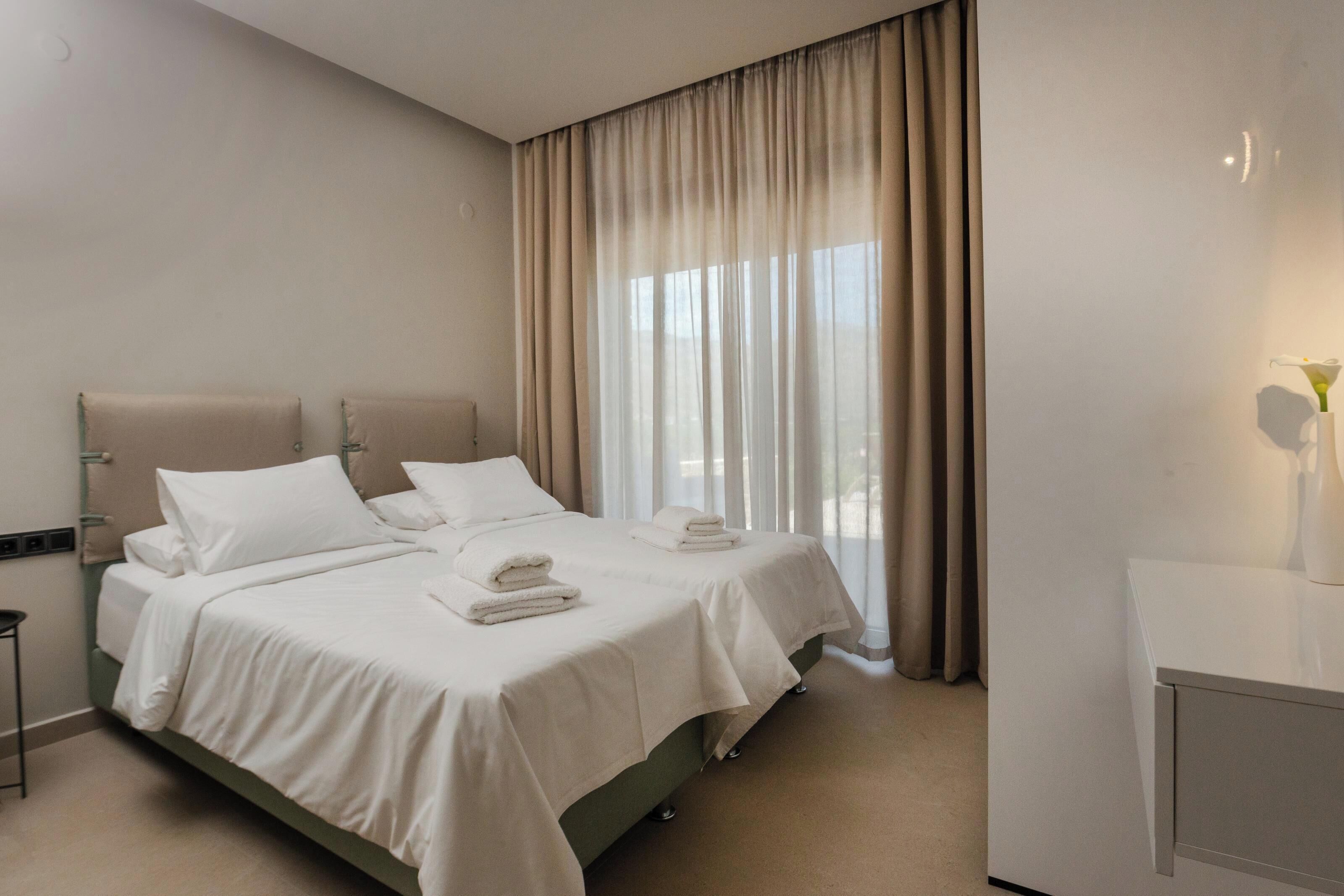 Une chambre d’hôtel avec un lit double, une table de chevet, un bureau et une grande fenêtre avec des rideaux.