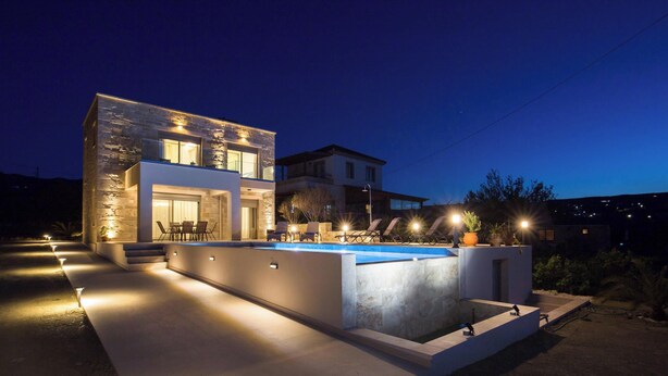A modern two-story house with a swimming pool, outdoor seating, and well-lit pathways.