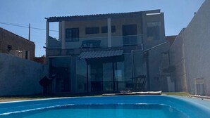 Una piscina con superficie de agua azul transparente, rodeada por un edificio residencial con techo plano y numerosas ventanas.