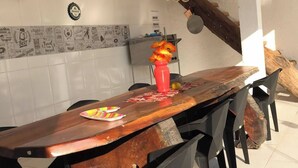Una larga mesa de comedor de madera con sillas negras, un jarrón rojo con flores y un letrero de Corona en la pared.