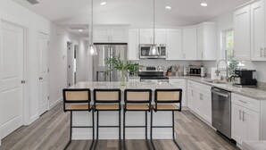 A modern kitchen with white cabinetry, stainless steel appliances, and a central island with bar stools.