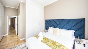 A hotel room with a bed, a headboard, a bedside table, a nightstand, a lamp, and a sign. - Modern Executive Unit (East London)