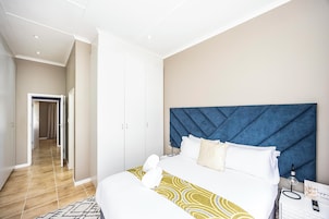 Una habitación de hotel con cama, cabecera, mesita de noche, lámpara y cartel.