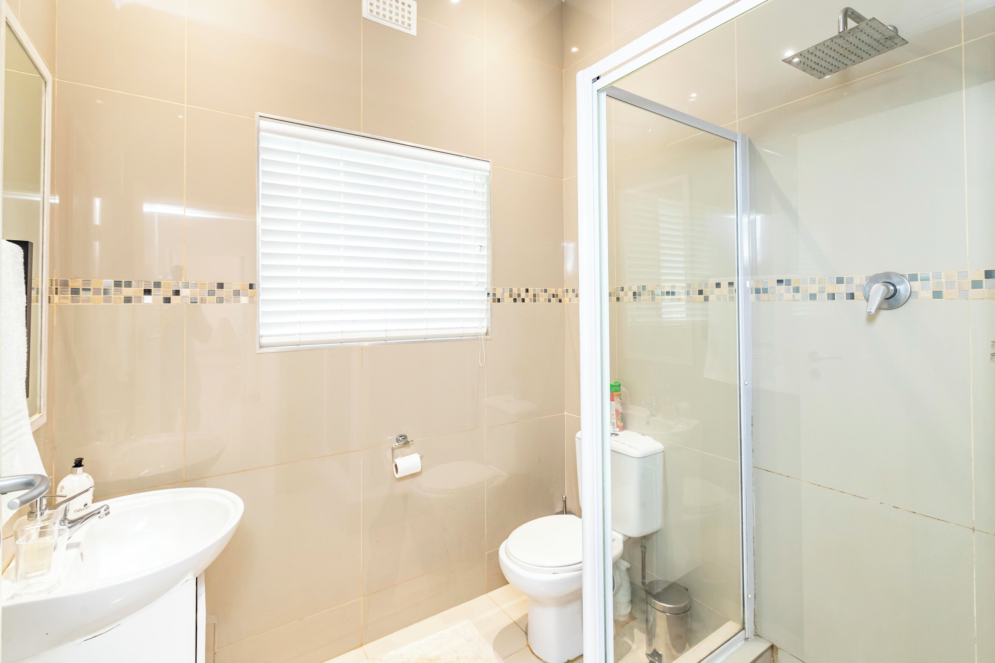 A bathroom with a glass-enclosed shower, a toilet, and a sink.