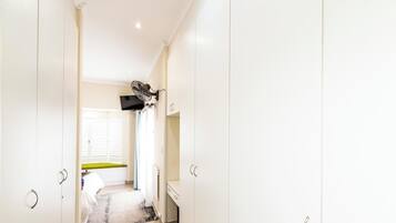 A hallway with white cabinets, a television mounted on the wall, and a window with blinds.