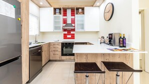 A modern kitchen with wooden cabinets, a stainless steel refrigerator, an oven, and a built-in island with bar stools. - Modern Executive Unit (East London)
